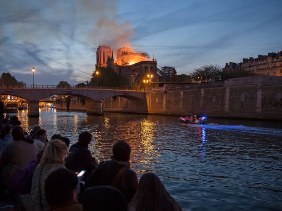 Menschen stehen am Ufer der Seine und blicken auf den Brand der Kathedrale Notre-Dame in Paris am 15. April 2019.